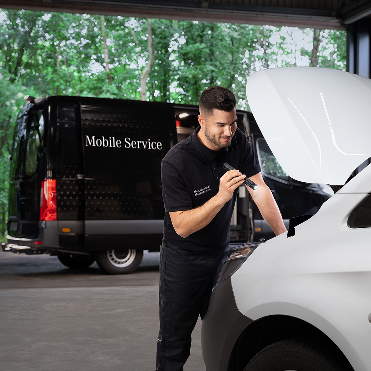 Wartungstechniker untersucht einen Motor bei geöffneter Motorhaube mit einer Taschenlampe